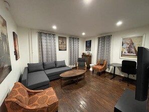 A living room with a sofa, coffee table, armchairs, a TV, and a radiator.
