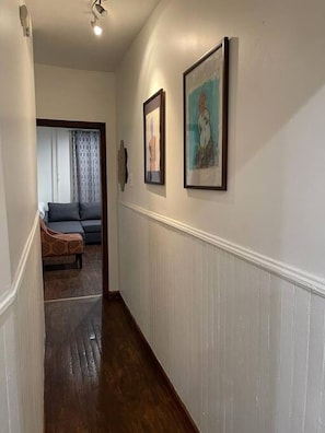 A hallway with a wooden floor, a sofa, and two framed artworks on the wall.