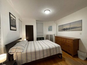 A bedroom with a bed, dresser, radiator, and artwork on the wall.