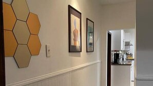 Un couloir avec des lambris blancs, une décoration murale hexagonale et des œuvres d’art encadrées.