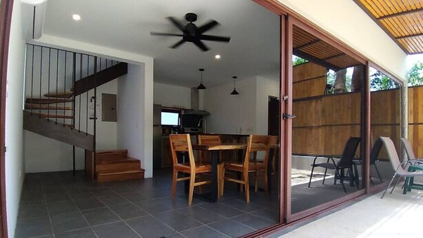 Un espacio interior amplio con una escalera, una mesa de comedor con sillas y un ventilador de techo.