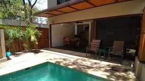 Una piscina con un patio cubierto, mobiliario exterior y vista al jardín trasero.