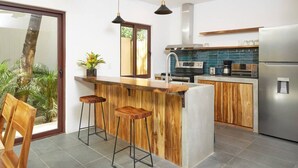 Una cocina moderna con una isla de madera, taburetes de bar, un refrigerador de acero inoxidable y un horno empotrado.