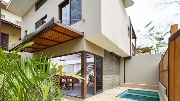 Una casa moderna de dos pisos con un porche cubierto, puerta de cristal y una pequeña piscina.