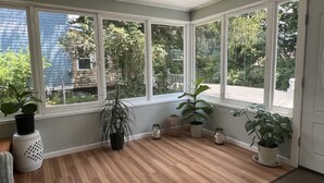 A sunroom with large windows, wooden flooring, and several potted plants.