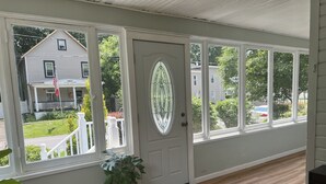 A room with a large window, a door with a glass panel, a potted plant, and a doormat.