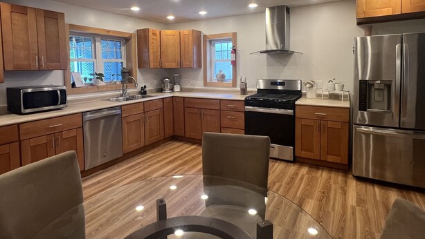 A modern kitchen with wooden cabinets, stainless steel appliances, and a glass dining table.