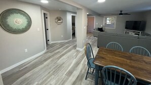 Une cuisine spacieuse avec une table et des chaises en bois, une grande assiette décorative accrochée au mur et un ventilateur de plafond.