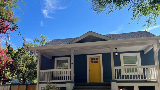 Une maison à deux étages avec une porte d’entrée jaune, des balustrades blanches et le numéro « 854 » sur la porte.