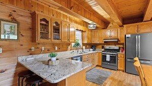 Eine Holzhüttenküche mit Granit Arbeitsplatten, Holzschränken, einem Edelstahlkühlschrank und einem eingebauten Backofen.