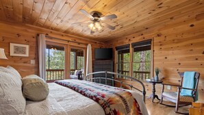 Ein Schlafzimmer einer Holzhütte mit einem Bett, einem Deckenventilator, einer Kommode und einem Schaukelstuhl.