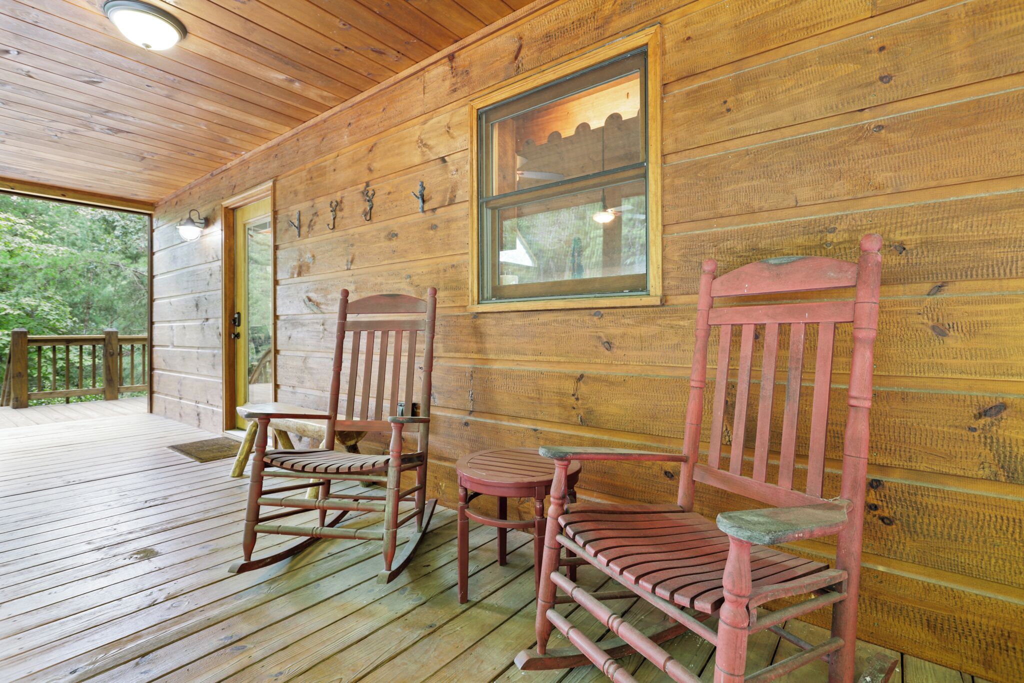 A wooden porch with rocking chairs and a table, wooden walls, and a window.