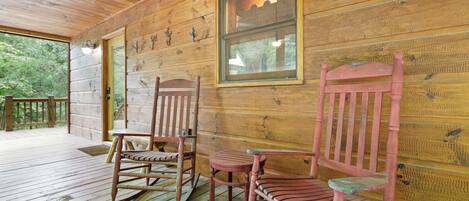 A wooden porch with rocking chairs and a table, wooden walls, and a window.