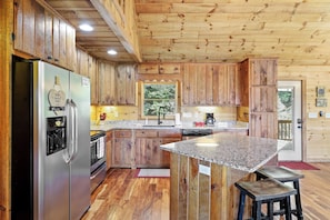 A kitchen with wooden cabinets, a stainless steel refrigerator, a granite countertop, and a wooden island with stools.