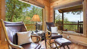 Une terrasse en bois avec deux fauteuils en cuir, une table avec une lampe et une vue sur les arbres.