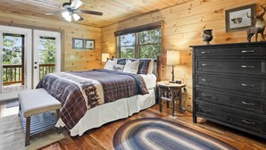 Une chambre dans une cabane en bois, comprenant un lit, un banc, une commode et un ventilateur de plafond.