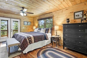 A wooden cabin bedroom with a bed, bench, dresser, and a ceiling fan.