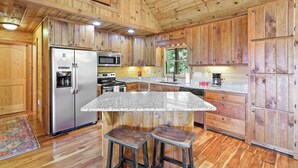 Une cuisine rustique aménagée dans une cabane en bois, avec un plan de travail en granit, des appareils en acier inoxydable et des tabourets en bois.