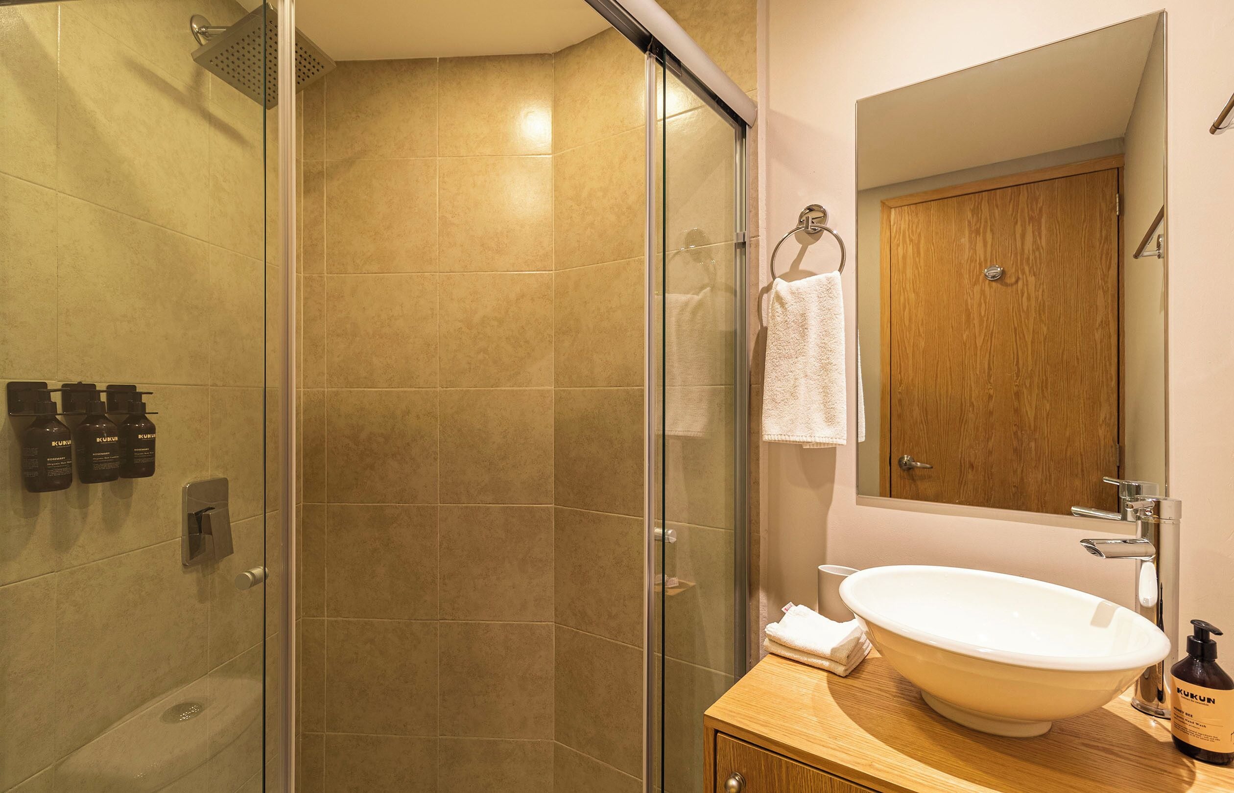 Een moderne badkamer met een glazen douchecabine, een houten wastafelmeubel met een wastafel en een spiegel erboven.
