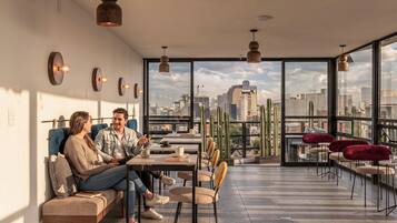 Un interior moderno con vista a la ciudad, que incluye un área de estar con una mesa, sillas y un sofá.