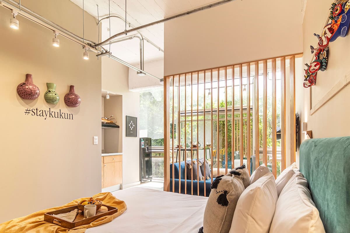 A modern hotel room with a bed, a sofa, a kitchen area, and a balcony with a view.