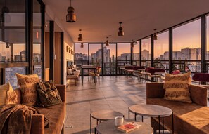 Un vaste salon sur le toit, offrant une vue sur la ville, et aménagé avec des canapés, des fauteuils et des tables.