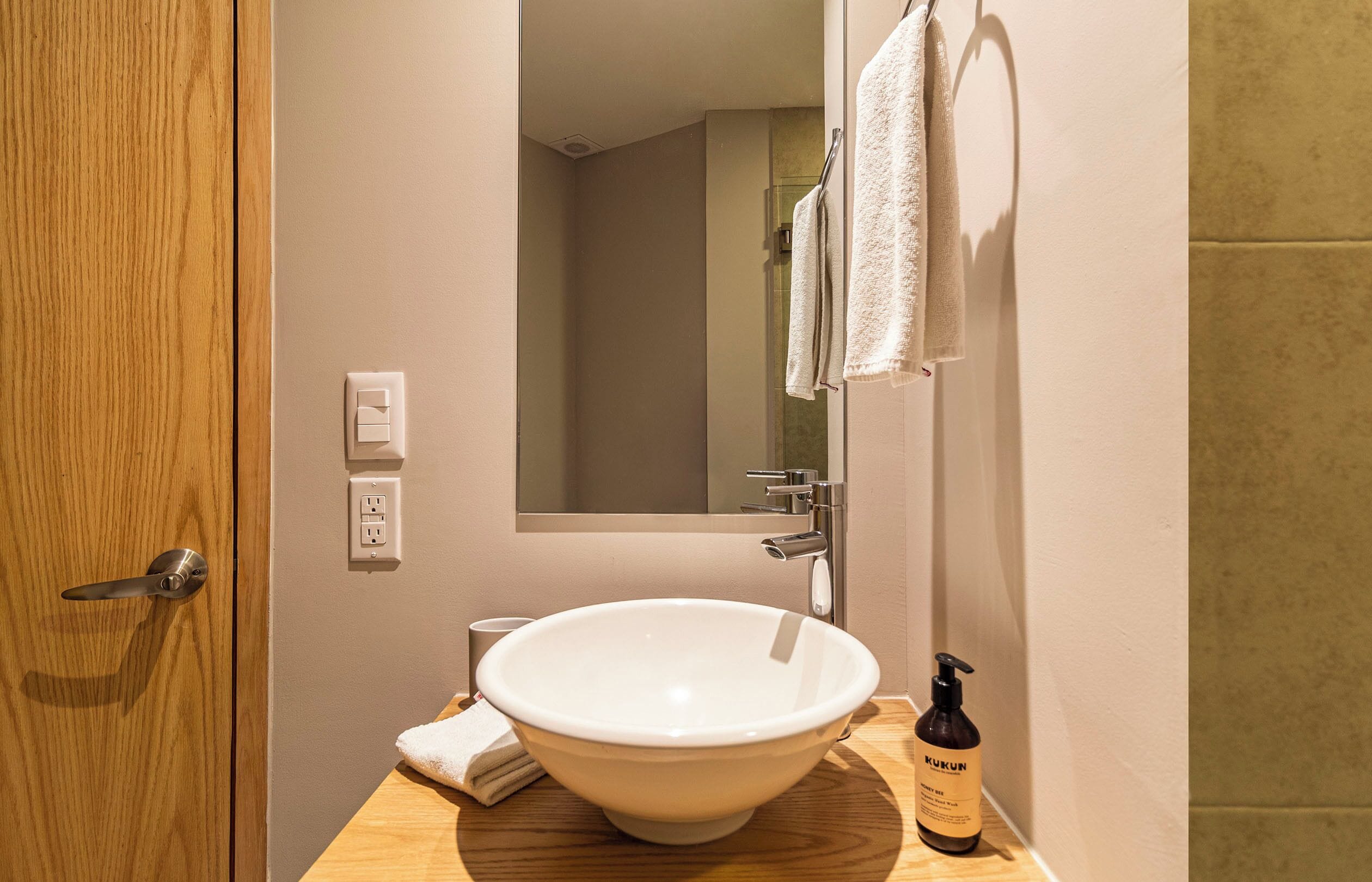 A bathroom with a white sink, a mirror, a towel, and a bottle of hand soap.