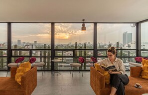 A spacious room with large windows offering a city view, a comfortable seating area with chairs and a sofa, and a person reading a book. - Kukun Insurgentes Roma (Mexico City)