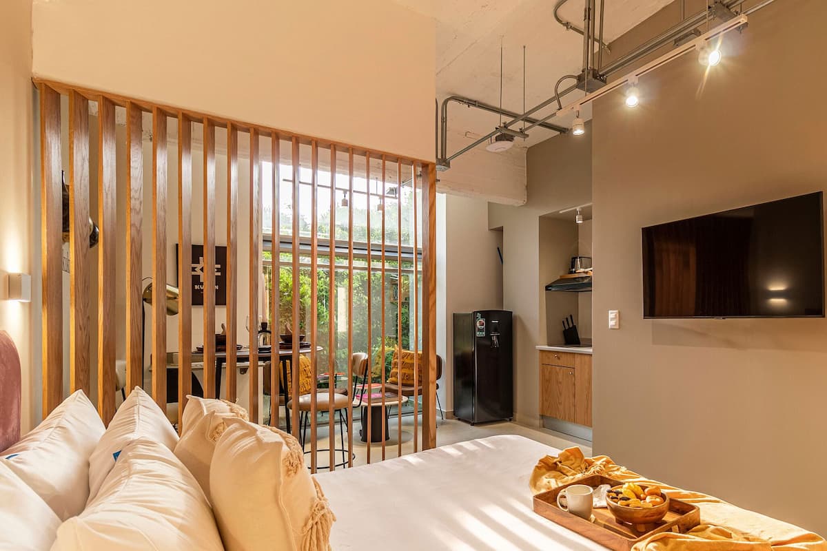 A modern bedroom with a bed, a wooden partition, a dining area, and a kitchen.