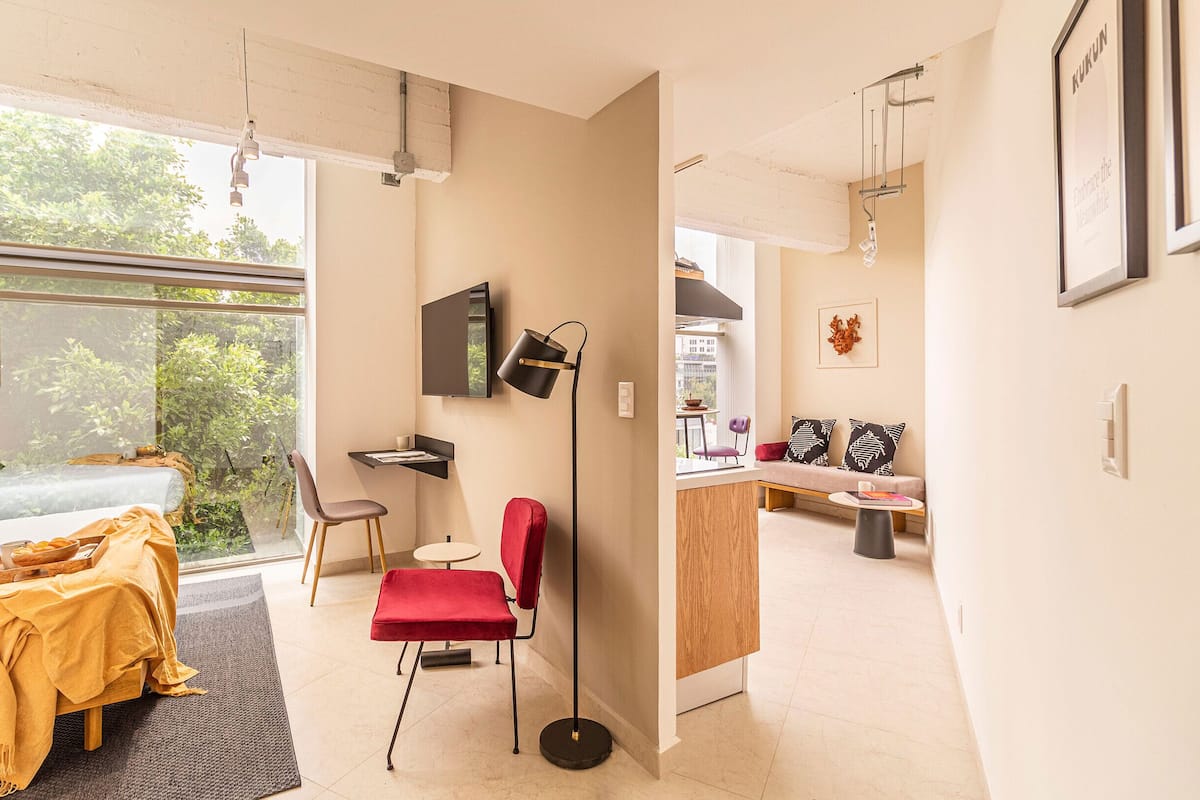 A modern living room with a sofa, a red chair, a small table, and a TV mounted on the wall.