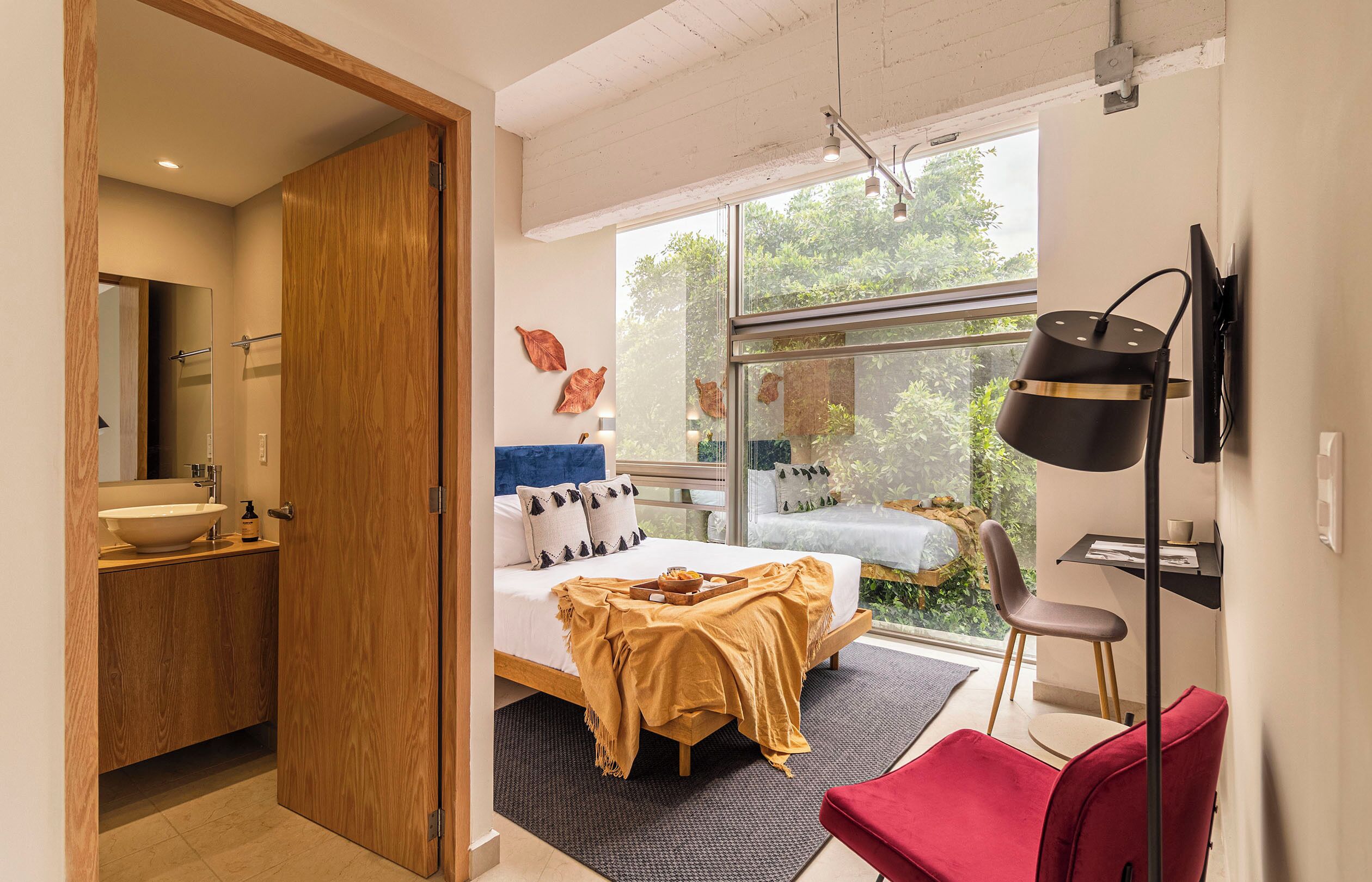 Een moderne slaapkamer met een groot raam, een bed met hoofdeinde, een nachtkastje en een rode stoel.