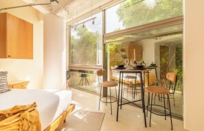 Ein modernes Schlafzimmer mit einem großen Bett, einem kleinen Tisch mit Stühlen und Blick auf Grün durch große Fenster.