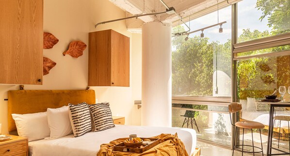 Un dormitorio moderno con una cama grande, cabecera de madera y vistas a la vegetación a través de un amplio ventanal.