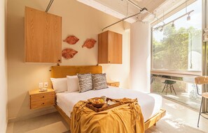 A bedroom with a bed, wooden headboard, bedside tables, and a window with a view of greenery. - Kukun Insurgentes Roma (Mexico City)