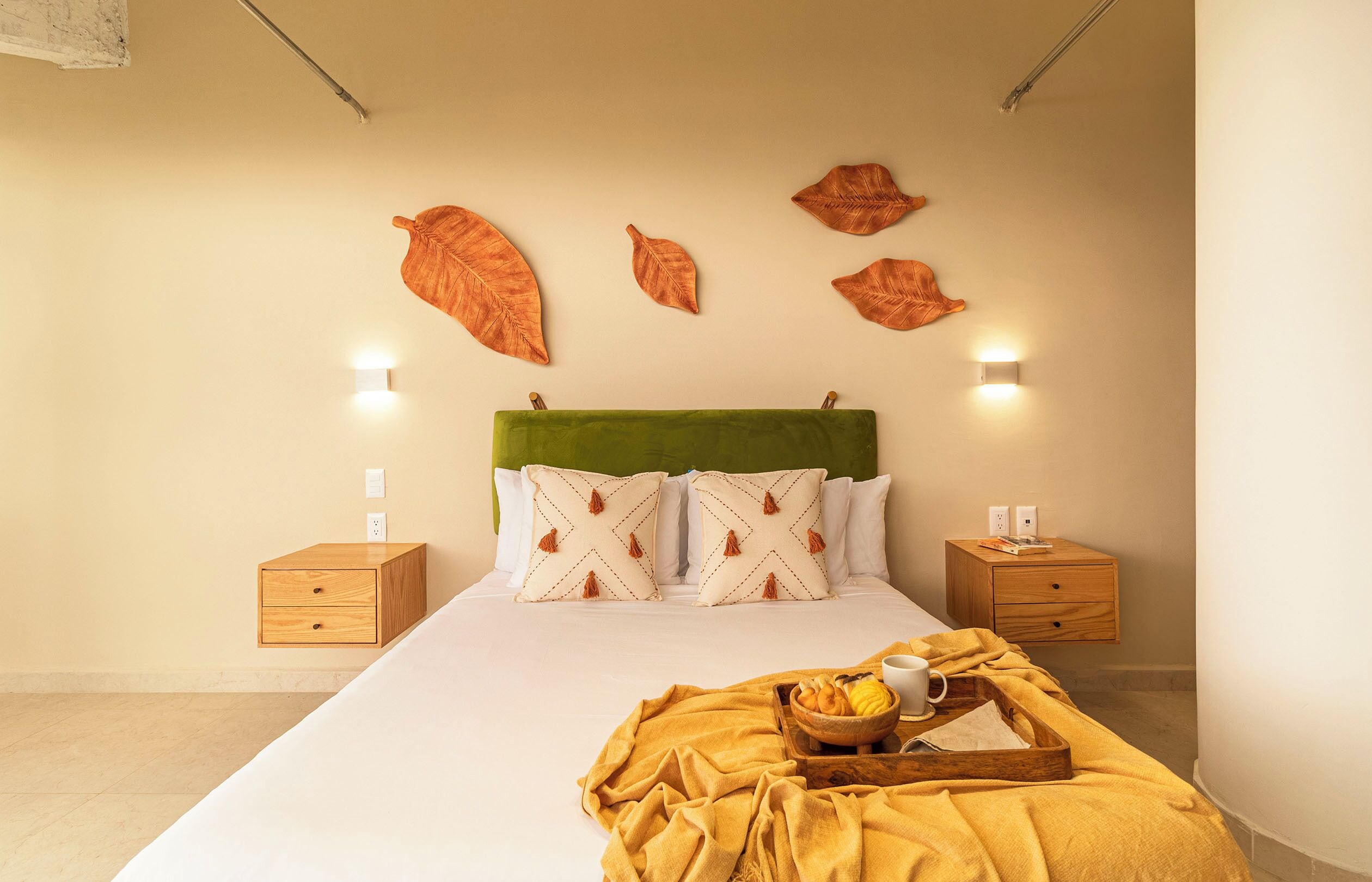 Une chambre d’hôtel avec un lit, deux tables de chevet, une tête de lit verte et des lampes fixées au mur.