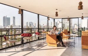 A spacious balcony with a city view, furnished with modern chairs and tables, and a person reading a book. - Kukun Insurgentes Roma (Mexico City)