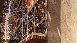 A modern building with a glass facade reflecting trees, a wooden deck, and a patterned wall. - Kukun Insurgentes Roma (Mexico City)