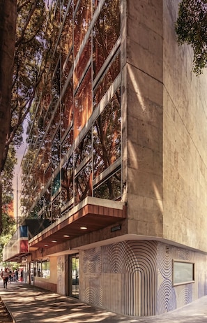 A modern building with a glass facade reflecting trees, a wooden deck, and a patterned wall. - Kukun Insurgentes Roma (Mexico City)