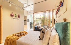 A modern hotel room with a bed, a wooden side table, a decorative wall, and a view through a glass partition. - Kukun Insurgentes Roma (Mexico City)