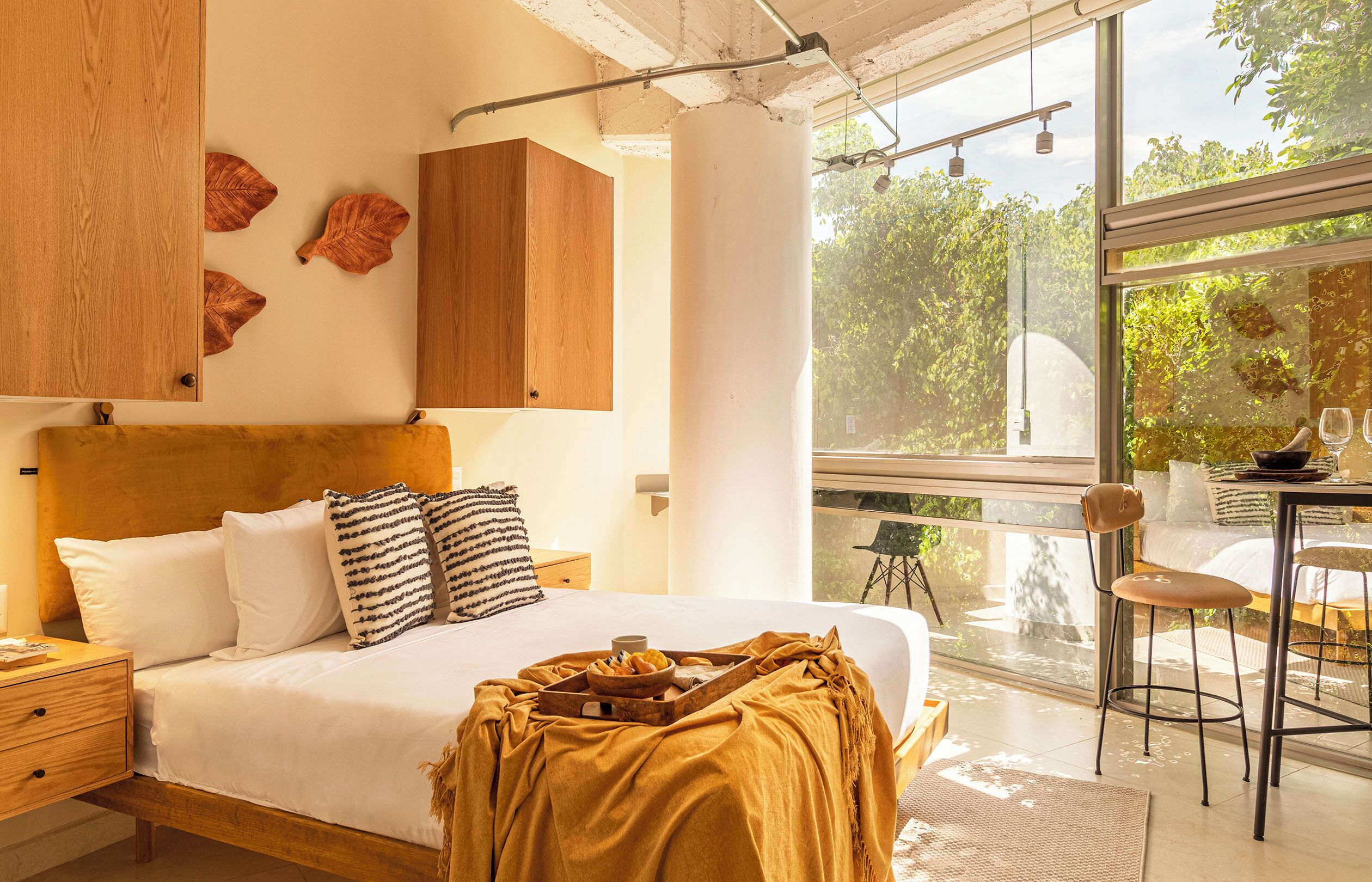 Une chambre moderne avec un grand lit, une tête de lit en bois et une vue sur la verdure grâce à une grande fenêtre.