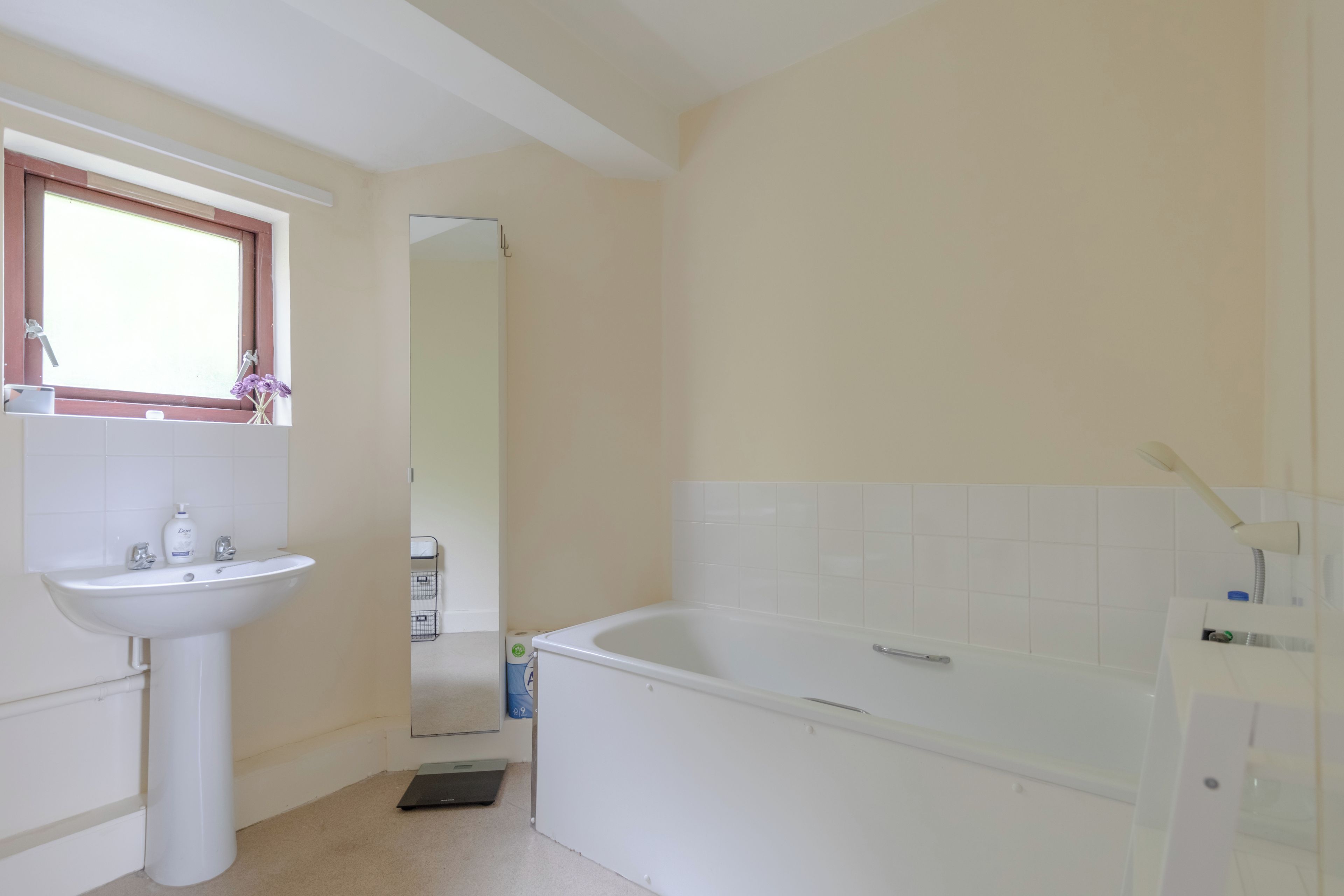 A bathroom with a white sink, a mirror, a bathtub, and a window.