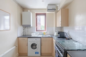 A compact kitchen with a washing machine, a coffee machine, and a window with a view of a building outside.