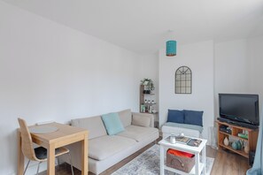 A modern living room with a sofa, a dining table, a TV, and a bookshelf. - Fantastically Located 1BD Flat in Islington (London)