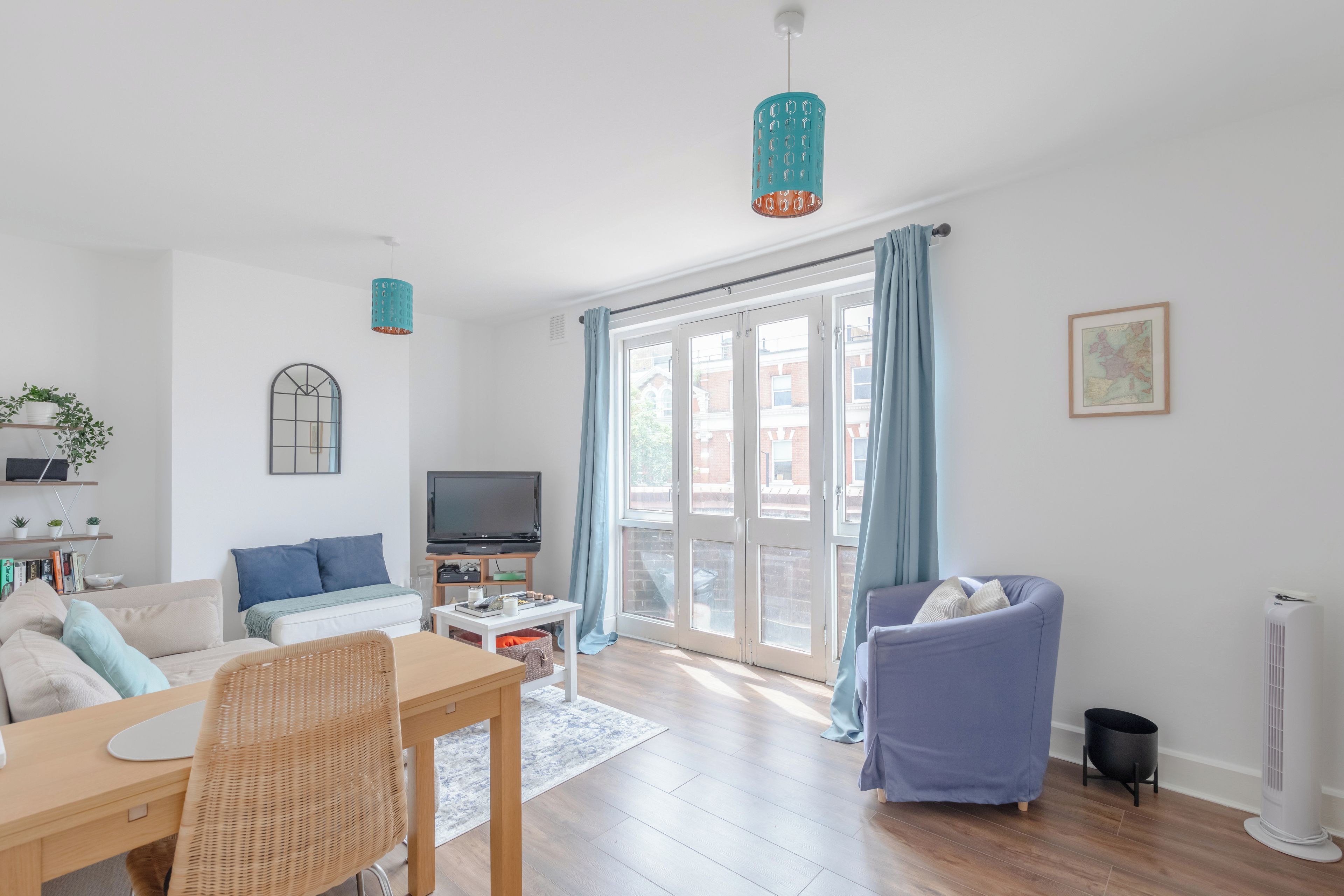 Een moderne woonkamer met een bank, een eettafel, een televisie en een groot raam met gordijnen.
