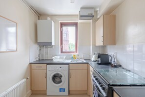 A compact kitchen with a washing machine, a coffee machine, and a window with a view of a building outside. - Fantastically Located 1BD Flat in Islington (London)