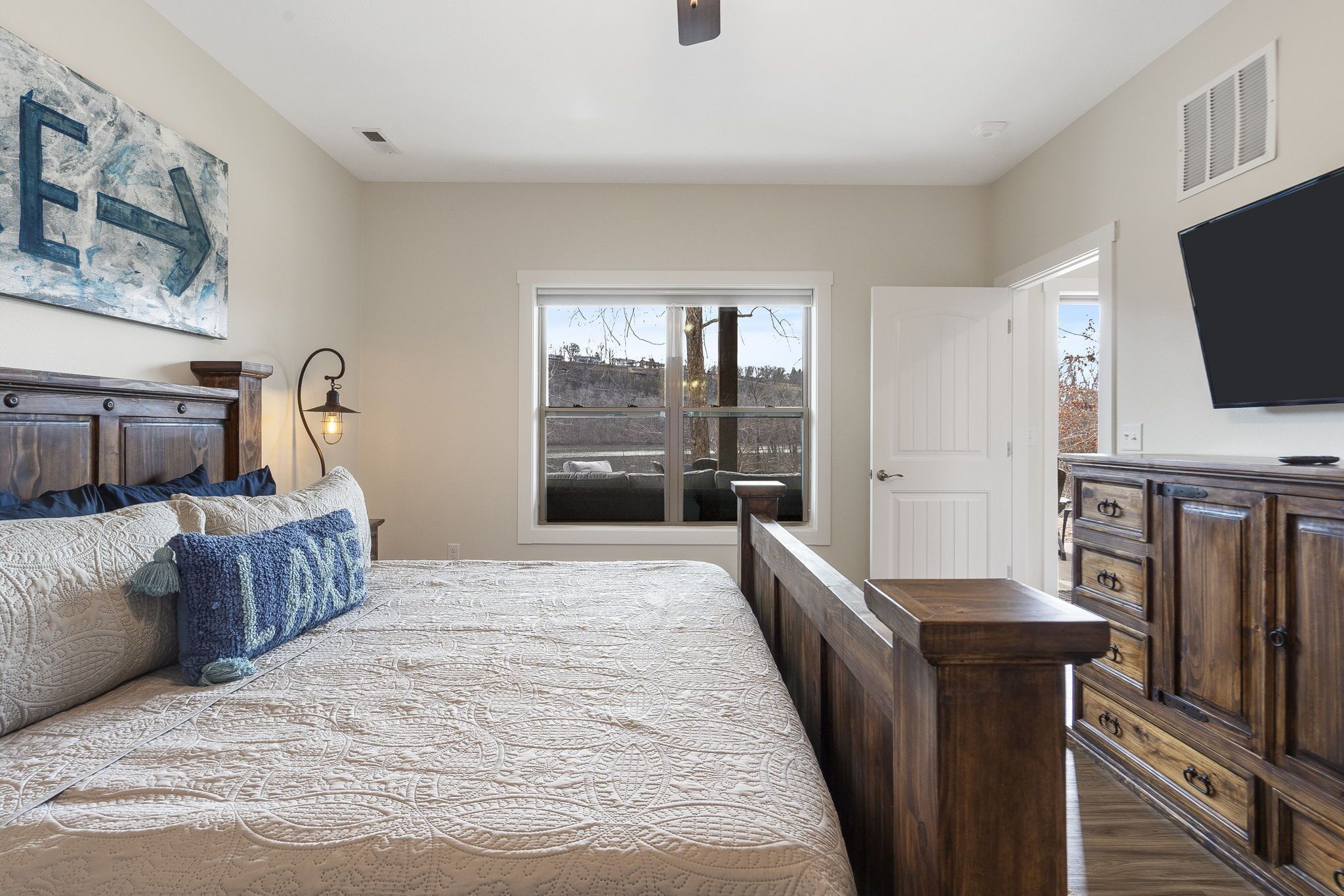 Une chambre avec un grand lit, une table de chevet, une commode, un téléviseur et une fenêtre donnant sur l’extérieur.