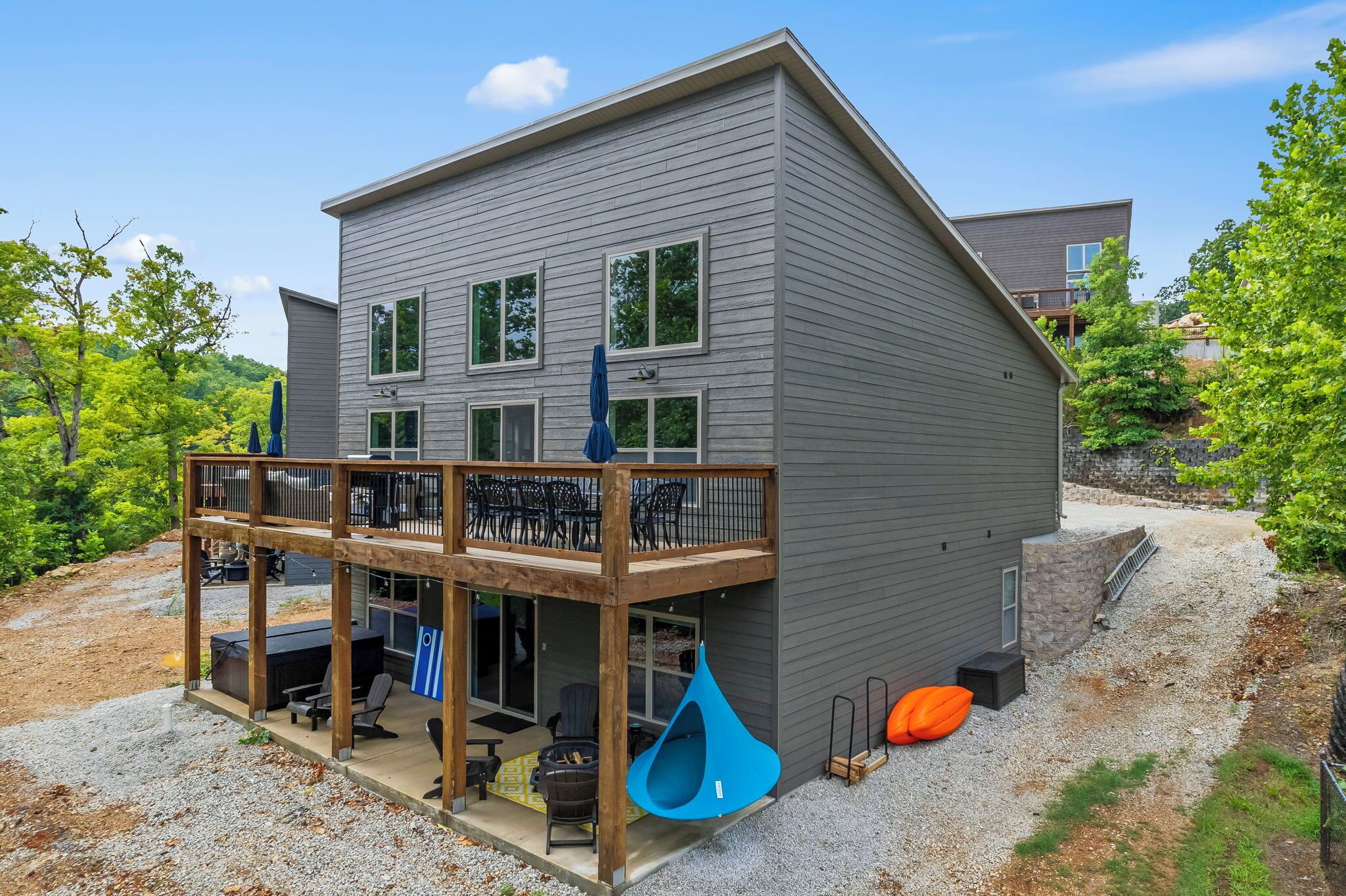 Une maison moderne à deux étages dotée d’un patio couvert, d’un espace salon extérieur et d’un fauteuil suspendu.