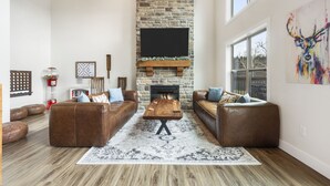 A living room with a stone fireplace, leather sofas, a coffee table, and a large window.