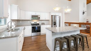 A modern kitchen with white cabinets, stainless steel appliances, granite countertops, and a wooden ceiling.