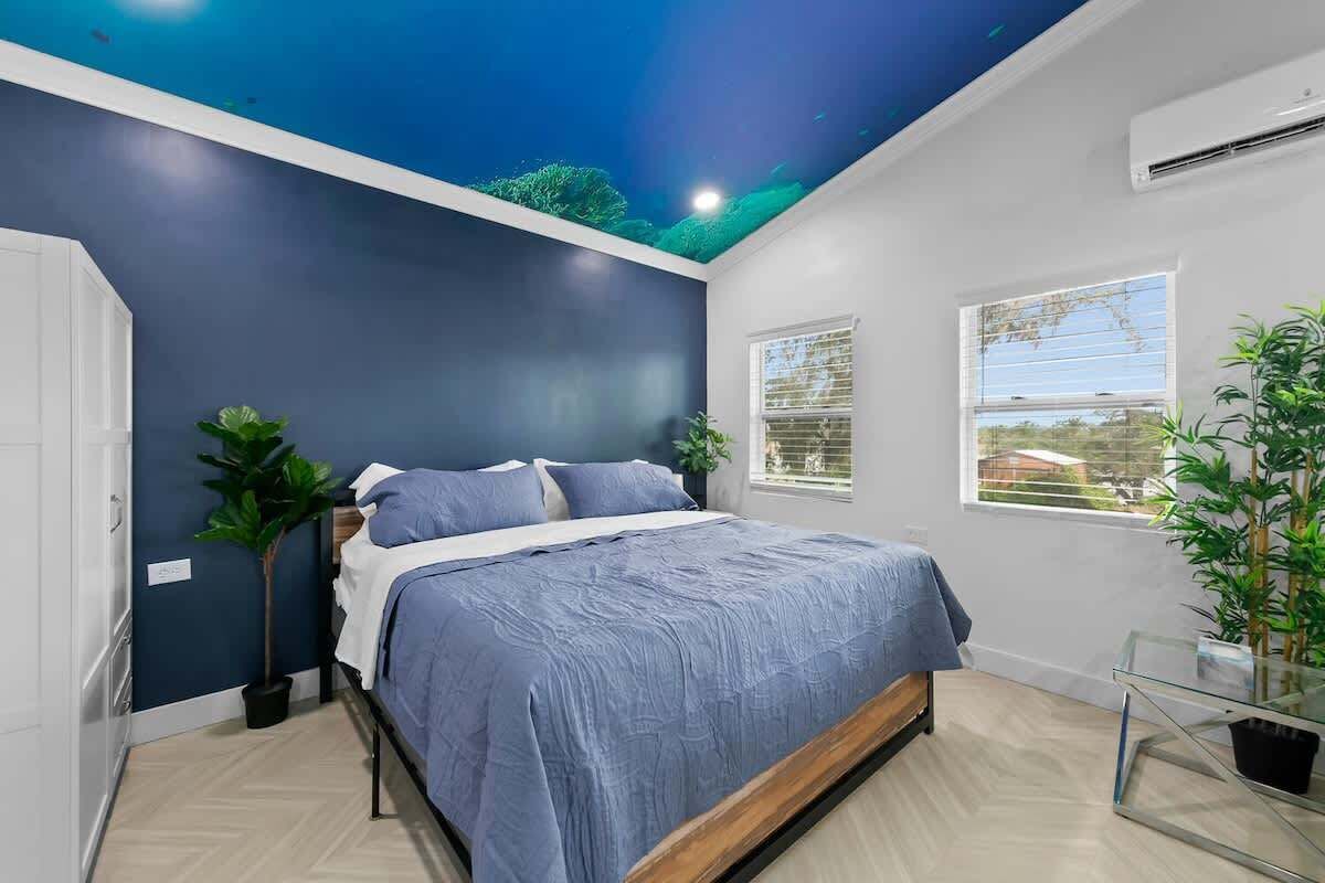 A bedroom with a bed, a window, and a ceiling with a painted sky.